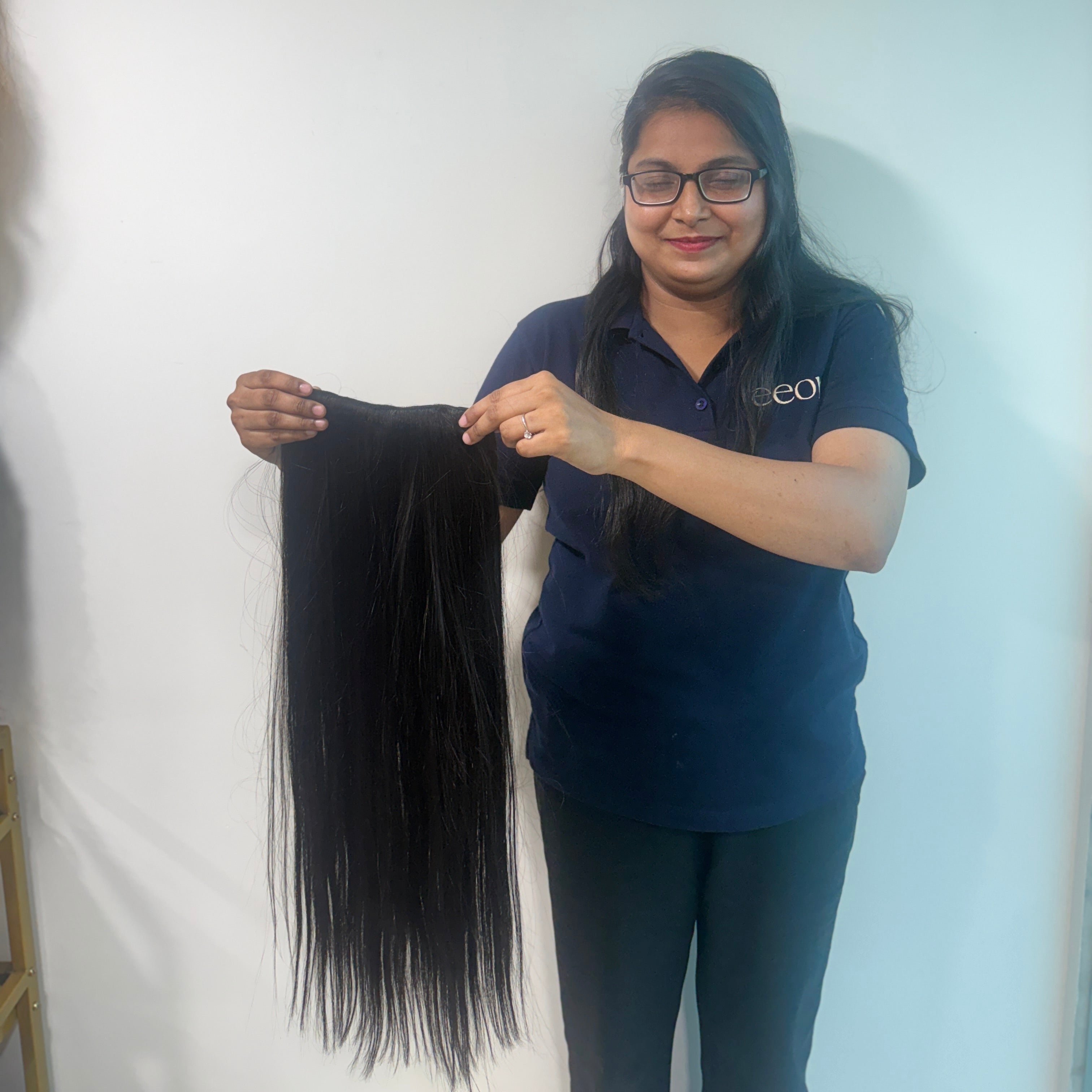 Person holding a long black hair extension against a white background