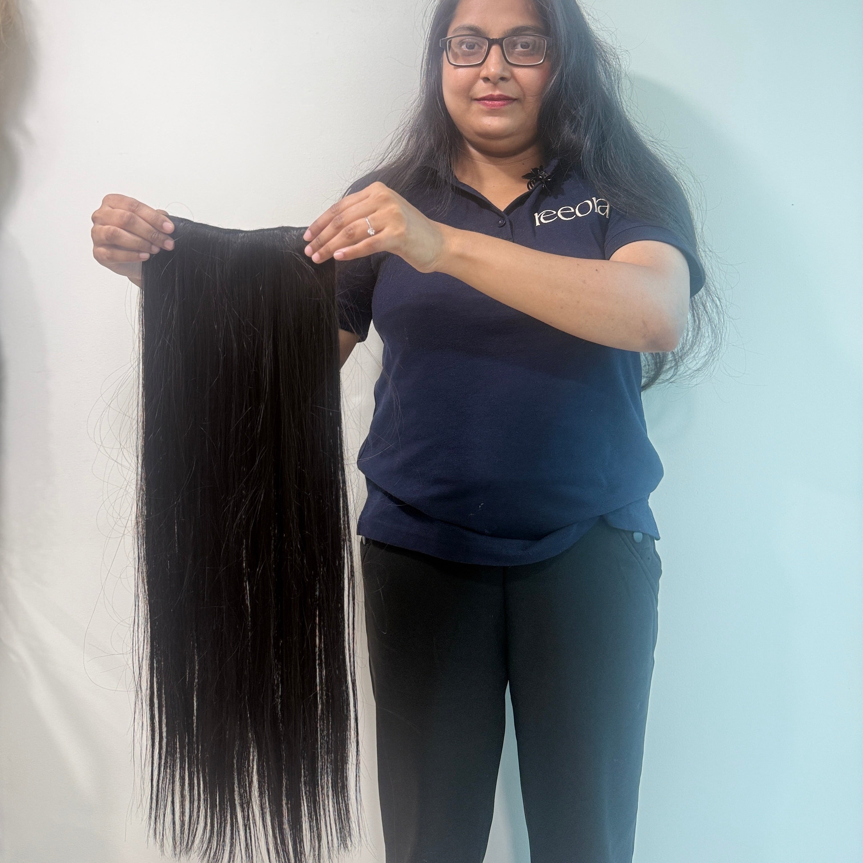 Person holding a long black hair extension against a plain background