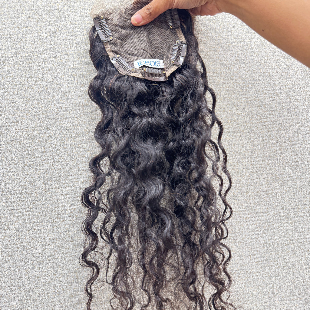 Curly hair extensions held by a hand on a light gray background