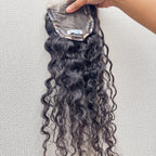 Curly hair extensions held by a hand on a light gray background