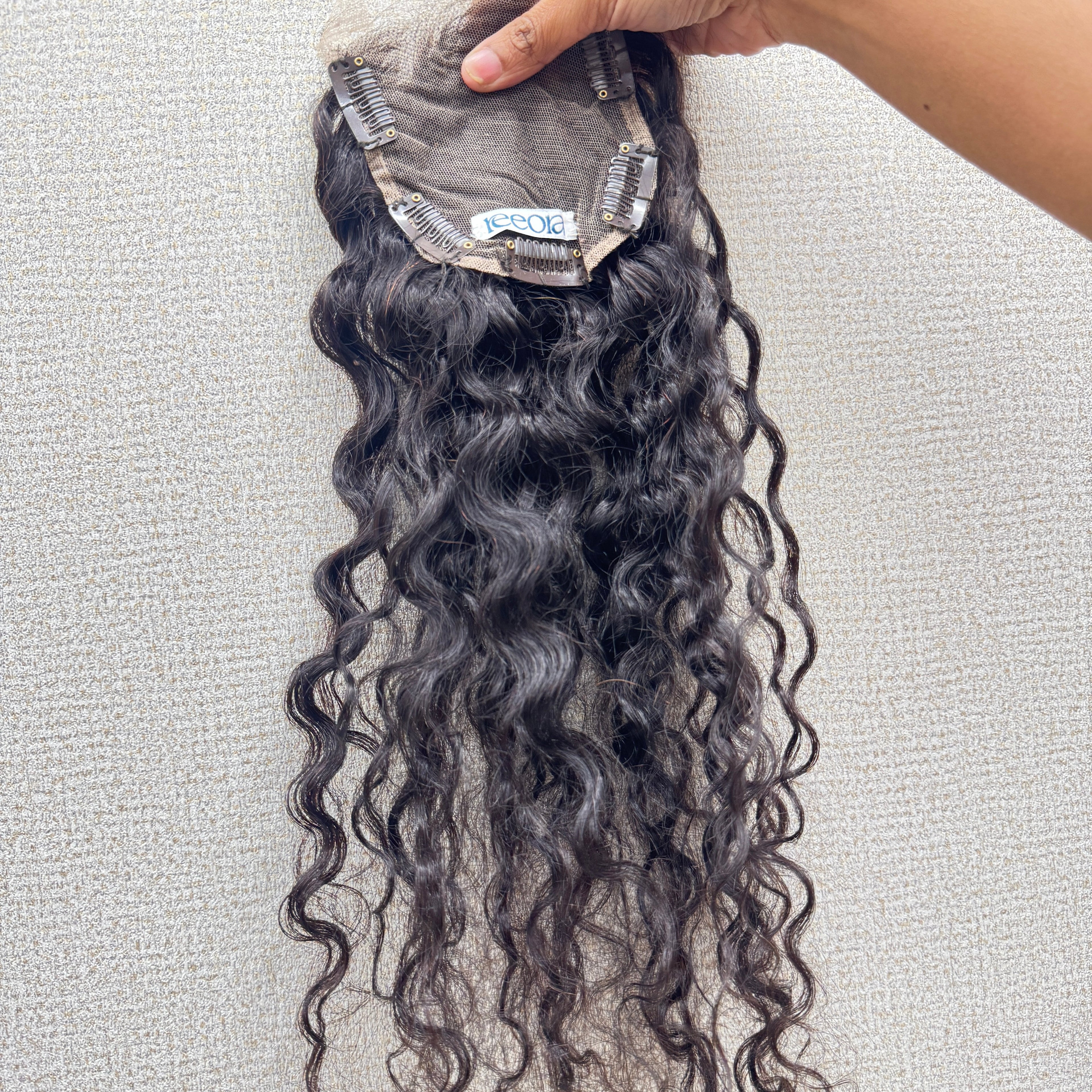 Curly hair extensions held by a hand on a light gray background