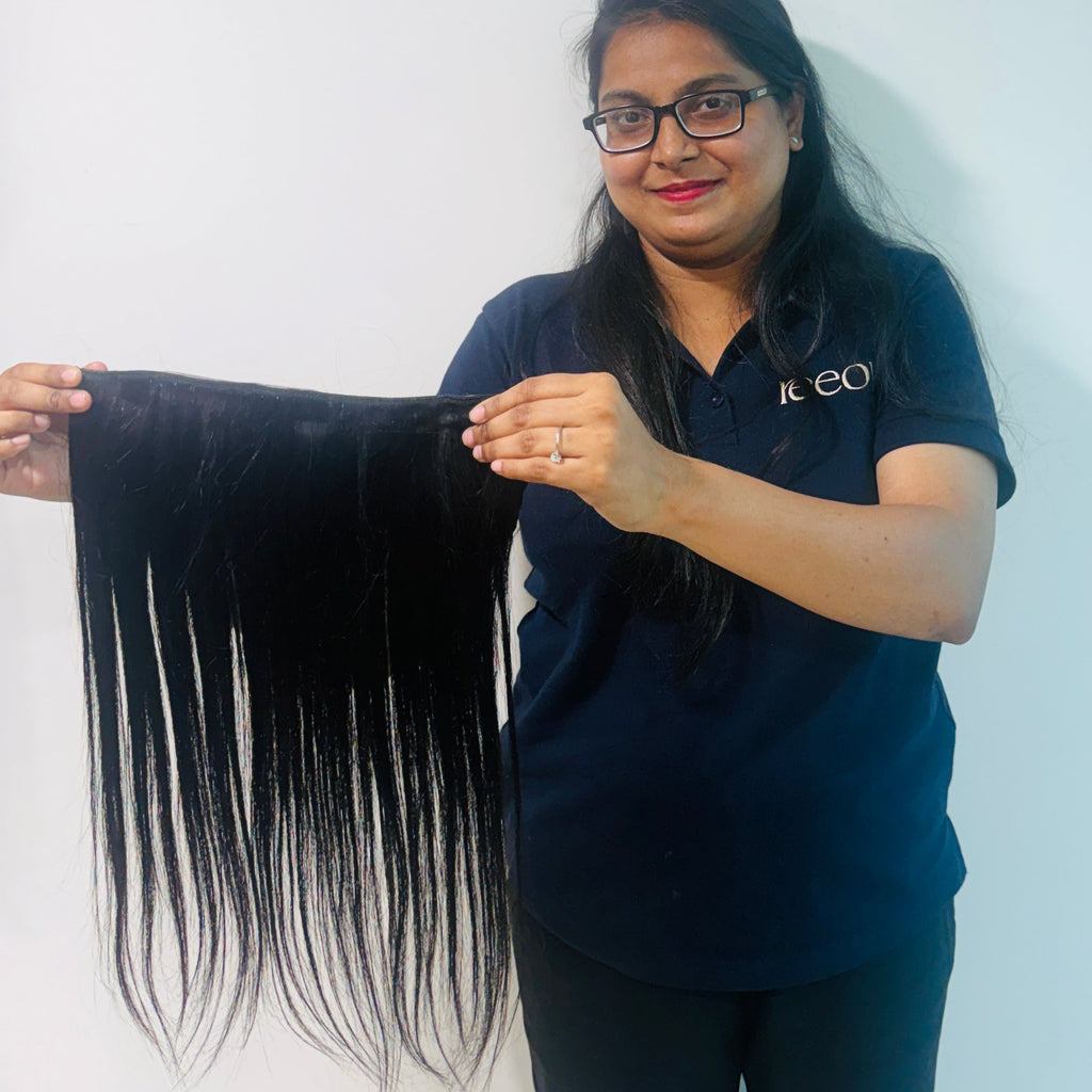Person holding a bundle of black hair extensions against a white background